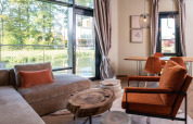 Modern glamping accommodation interior with large windows, comfortable seating and warm earthy tones.