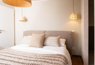 Knusse glamping accommodatie met comfortabel bed, zachte kussens en sfeervolle hanglampen.