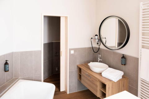Moderne badkamer in glamping-accommodatie met ronde spiegel, houten wastafel en stijlvolle badkuip.