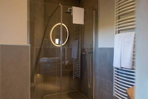 Moderne douche in een glamping-accommodatie met glazen deur, verlichte spiegel en handdoekenrek.