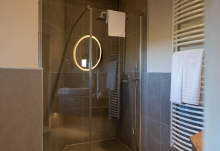 Moderne douche in een glamping-accommodatie met glazen deur, verlichte spiegel en handdoekenrek.