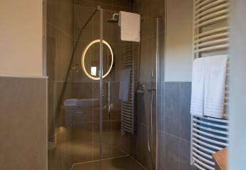 Modern shower in a glamping accommodation with glass door, illuminated mirror, and towels on a heater.