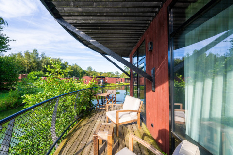 Houten terras bij een glamping-accommodatie, met stoelen, uitzicht op meer en groene natuur.