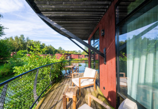 Houten terras bij een glamping-accommodatie, met stoelen, uitzicht op meer en groene natuur.