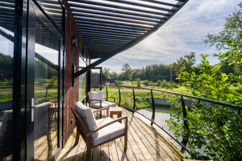 Zonnig terras bij een glampingaccommodatie met comfortabele stoelen en uitzicht op een groene vijver.