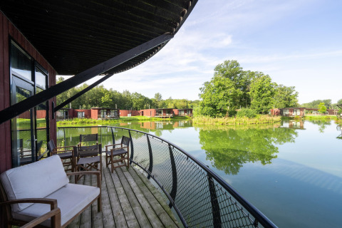 Uitzicht vanaf een lodge-balkon met stoelen en bank, uitkijkend op een serene vijver en groene omgeving.