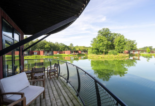 Uitzicht vanaf een lodge-balkon met stoelen en bank, uitkijkend op een serene vijver en groene omgeving.