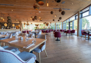 Licht en modern restaurant bij een glampingaccommodatie met grote ramen en stijlvolle inrichting.