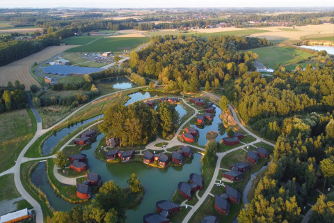 Luchtfoto van een lodge met kleine huisjes aan vijvers, omgeven door groene velden en bossen.