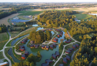 Luchtfoto van een lodge met kleine huisjes aan vijvers, omgeven door groene velden en bossen.