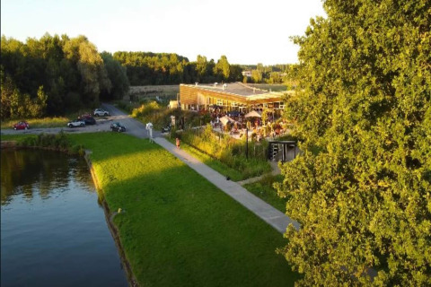 Glampinglocatie met terras, bezoekers en veel groen, gelegen aan een vijver in het avondzonnetje.
