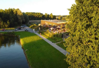 Scenic glamping site with a lively café, outdoor seating, green landscape, and a nearby pond at sunset.