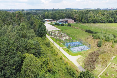 Luftfoto af glampingområde med tennisbaner, have og moderne bygninger omgivet af frodig skov.