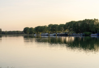 Scenic view of tranquil water and houseboats along a tree-lined shore at sunset at a glamping site.