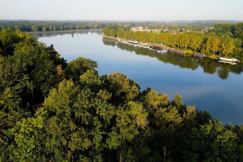 Uitzicht op een rustige rivier, omgeven door bomen en woonboten, genomen vanaf een glampinglocatie.