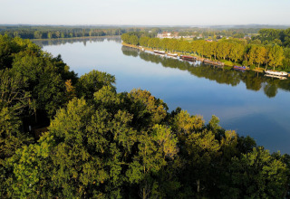 Uitzicht op een rustige rivier, omgeven door bomen en woonboten, genomen vanaf een glampinglocatie.