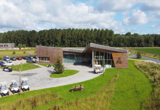 Moderne glamping-accommodatie met houten gevel, golfkarretjes en groene omgeving bij blauwe lucht