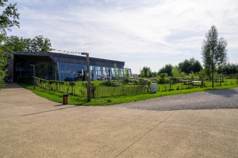 Foto van een moderne glamping-accommodatie met glazen gevel en groene tuin onder een halfbewolkte lucht.