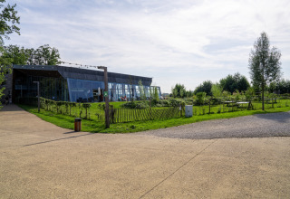 Foto van een moderne glamping-accommodatie met glazen gevel en groene tuin onder een halfbewolkte lucht.