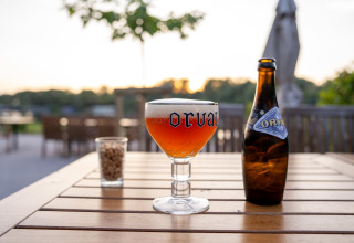 Orval beer in a branded glass and bottle with a snack outside on a wooden table at a glamping site.