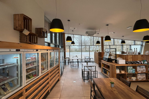 Moderne caféruimte bij een glamping, met houten meubilair, grote ramen en rustieke verlichting.