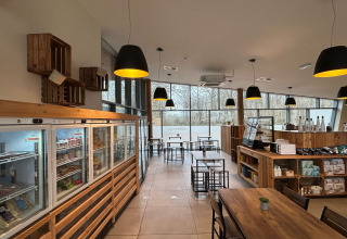 Moderne caféruimte bij een glamping, met houten meubilair, grote ramen en rustieke verlichting.