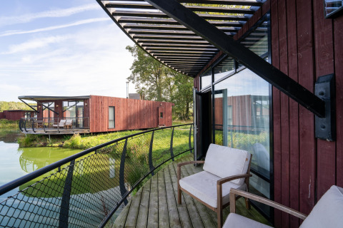Foto van een moderne lodge met houten terras, zitstoelen en uitzicht op water en andere lodges.