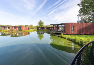 Moderne glampinghuisjes van hout aan een meer, omgeven door natuur en weerspiegeld in het water.