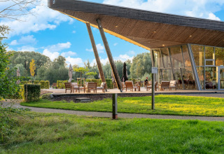 Moderne glampingaccommodatie met terras, grote ramen en uitzicht op groene natuur en bomen op de achtergrond.