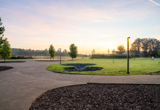 Uitzicht op een glampingterrein bij zonsopkomst met grasvelden, kronkelende paden en moderne verlichting.
