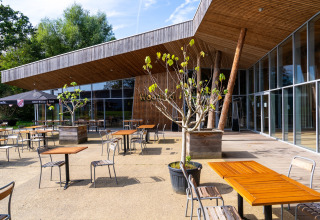 Buiten eetgedeelte bij een glamping-accommodatie met modern houten gebouw, tafels en bomen.