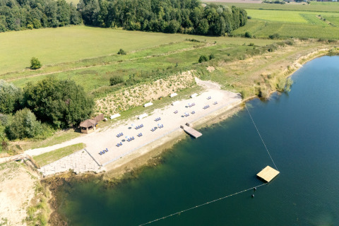 Luchtfoto van een glampinglocatie aan een meer met strandstoelen en omliggende groene velden.