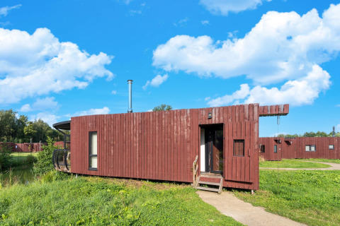Moderne glampingaccommodatie met houten buitenkant, omgeven door grasland onder een heldere blauwe lucht.