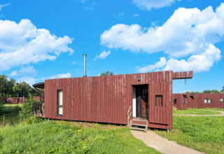 Moderne glampingaccommodatie met houten buitenkant, omgeven door grasland onder een heldere blauwe lucht.