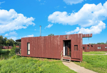 Modern glamping cabin with a wooden exterior, set in grassy surroundings under a bright blue sky.