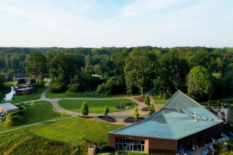 Aerial view of a glamping site featuring modern lodges, winding paths, and lush greenery near a forest.