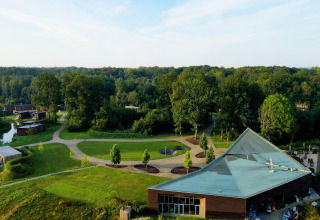 Aerial view of a glamping site featuring modern lodges, winding paths, and lush greenery near a forest.
