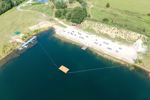 Luchtfoto van een glamping-accommodatie met zandstrand, ligstoelen, meer en vliegtuigen in het groen.