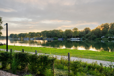 Uitzicht op een rustige plas bij zonsondergang vanaf een glamping-accommodatie met boten en groen.