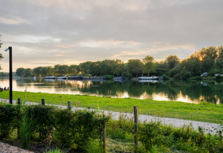 Uitzicht op een rustige plas bij zonsondergang vanaf een glamping-accommodatie met boten en groen.