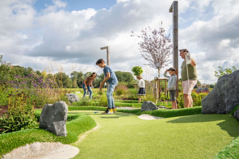 Gezin speelt minigolf op een groene baan bij een glamping-accommodatie onder een bewolkte lucht.