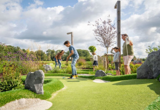 Gezin speelt minigolf op een groene baan bij een glamping-accommodatie onder een bewolkte lucht.