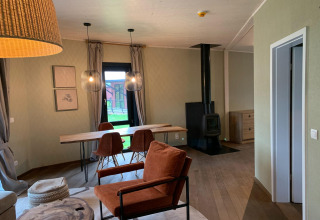 Moderne lodge-interieur in The Large Leaf by YourNature met houtkachel, eethoek en uitzicht op de tuin.