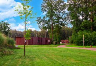 Foto van een lodge omgeven door groene bomen en gras, blauwe lucht en kronkelende paden ervoor.