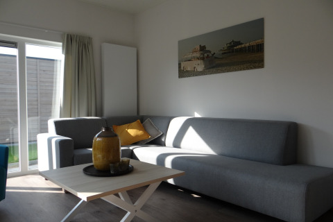 Moderne woonkamer in Breeduyn Village 3, België, met grijze banken, salontafel en zonlicht door grote ramen.