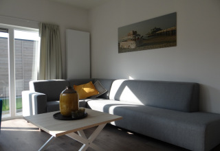 Moderne woonkamer in Breeduyn Village 3, België, met grijze banken, salontafel en zonlicht door grote ramen.