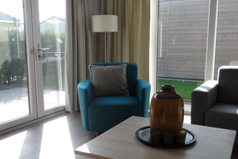 Woonkamer in Breeduyn Village 3 lodge in België met blauwe stoel, grote ramen en veel daglicht.