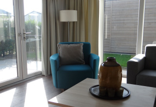 Woonkamer in Breeduyn Village 3 lodge in België met blauwe stoel, grote ramen en veel daglicht.