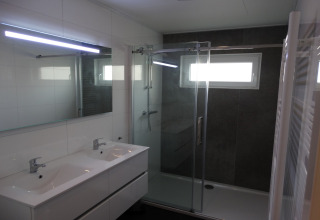 Moderne badkamer met dubbele wastafel, grote spiegel, glazen douche en raam in Breeduyn Village 3, België.