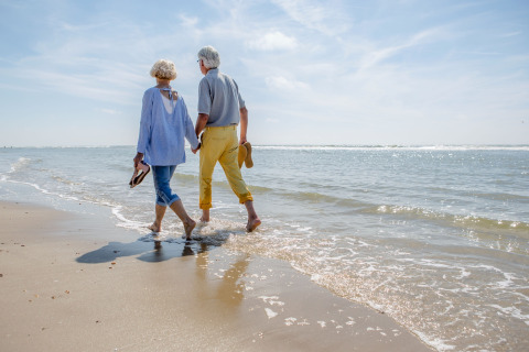 Ouder echtpaar loopt hand in hand op het strand bij Breeduyn Village 3 in België, zonnig weer.